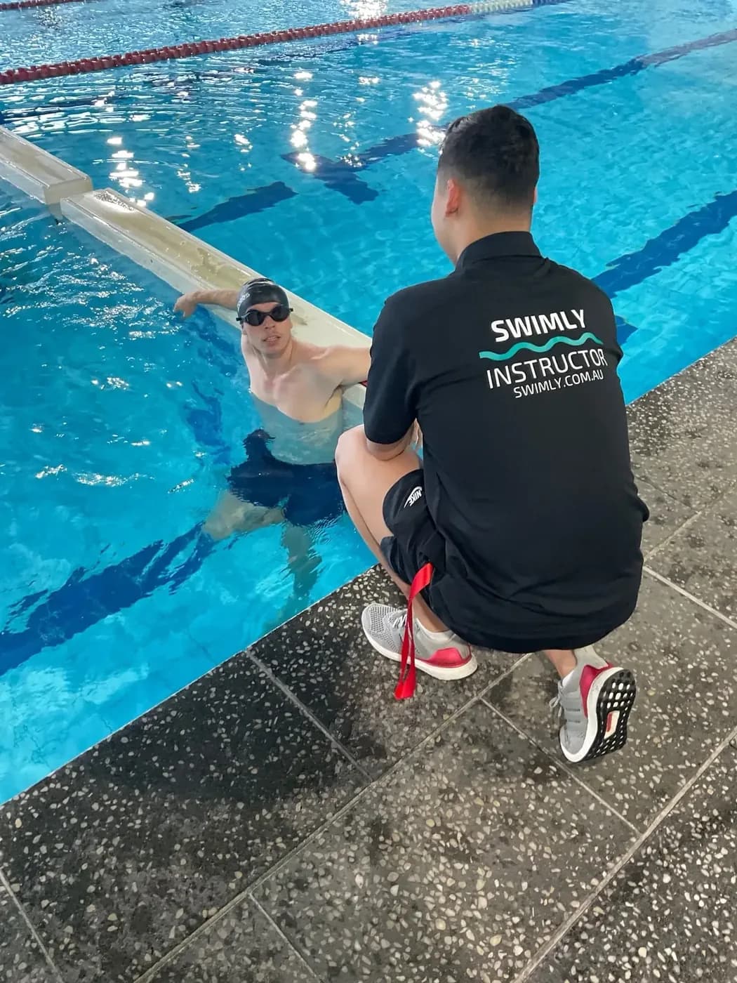A Swimly instructor talking with an adult swimmer at the wall