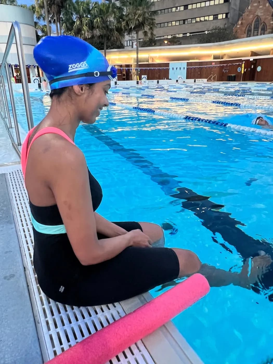 An adult sitting at the pool edge with a noodle before a session